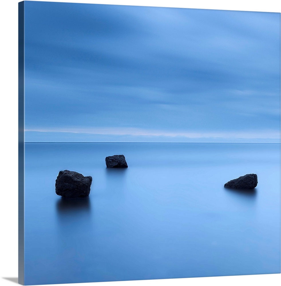 A zen calm minimal minimalist cool deep blue image of three rocks in a flat calm sea.