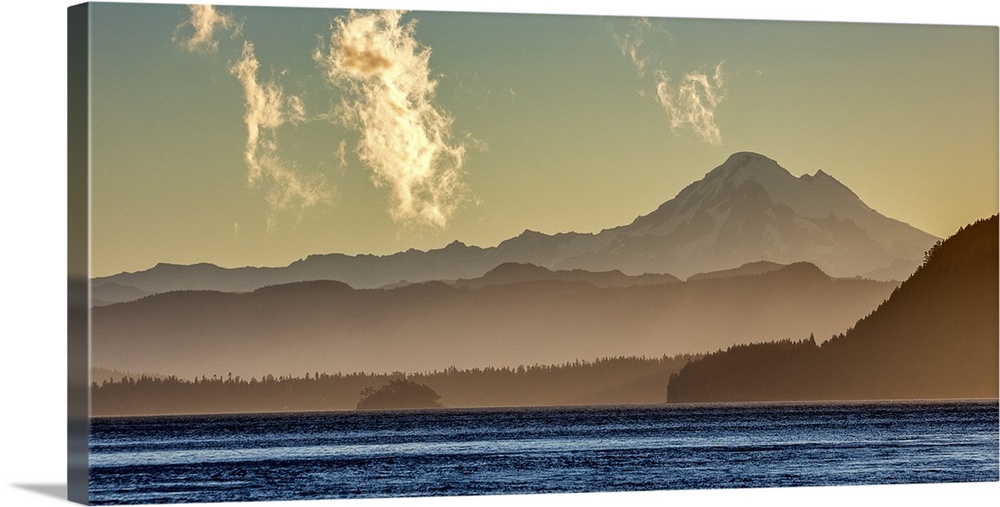 Mist surrounding the mountains on the Washington coast in dim sunlight with the bright blue ocean in the foreground.
