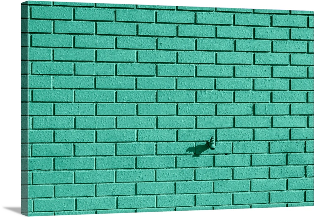 A faucet sticking out of a teal painted brick wall.