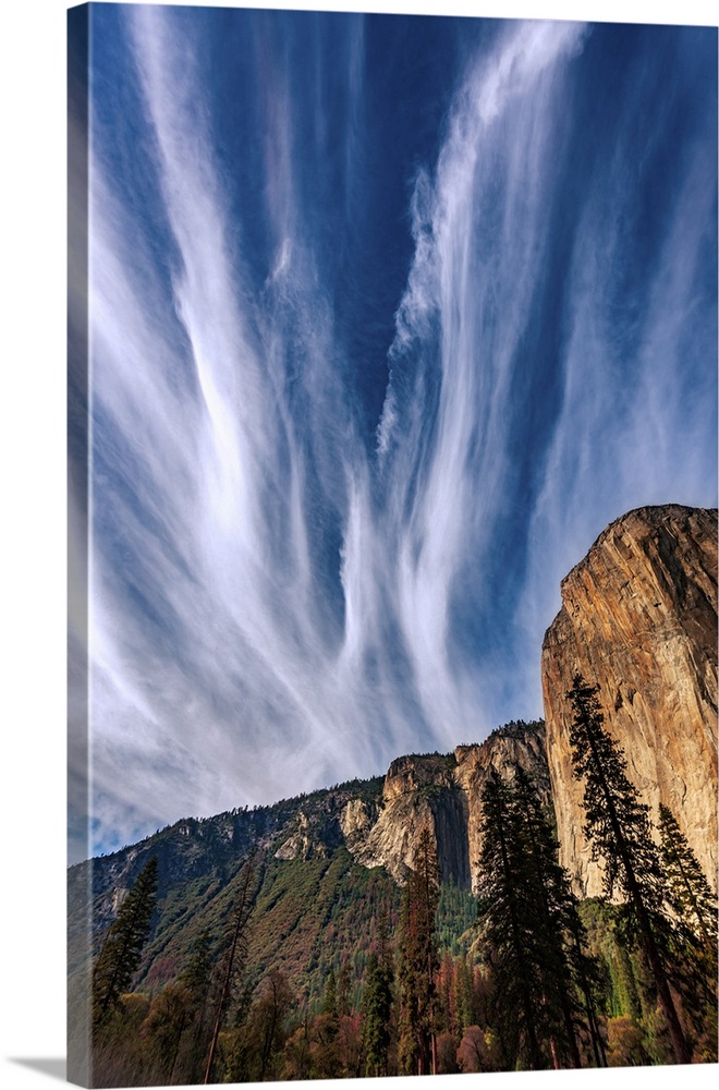 This picture features clouds dramatically streaking the blue sky fanning out above Yosemite's El Capitan cliff.