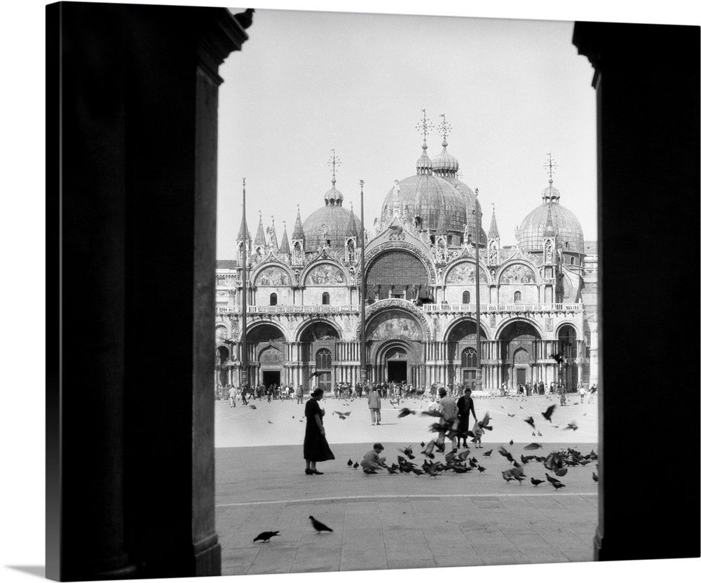 1920s 1930s View Through Doorway To People Feeding Pigeons In Front Of St. Marks Cathedral Venice Italy.