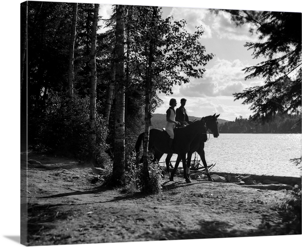 1930s Silhouetted Anonymous Man and Woman Riding Horses Through Wooded Area Along Side Of Lake.