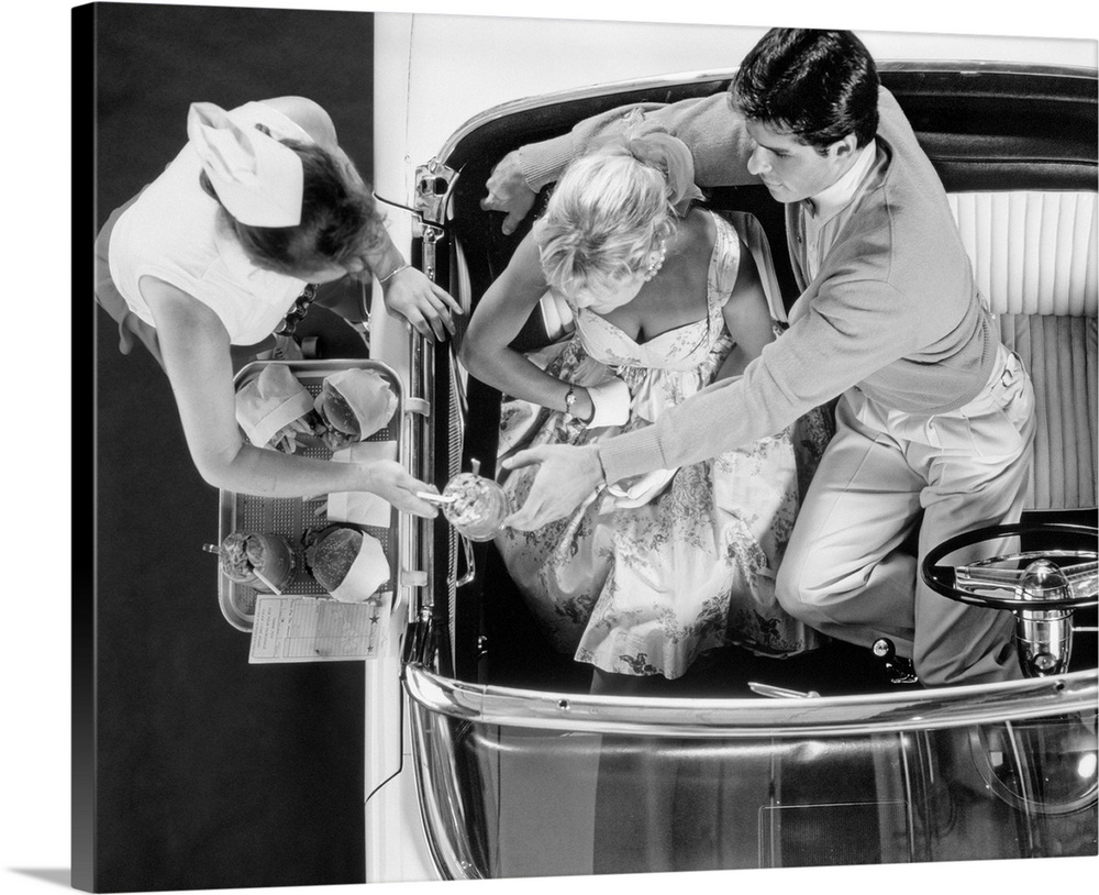 1950s Drive-In Restaurant Carhop Waitress On Roller Skates Serving Couple In 1955 T-Bird Car Burgers And Milkshakes.