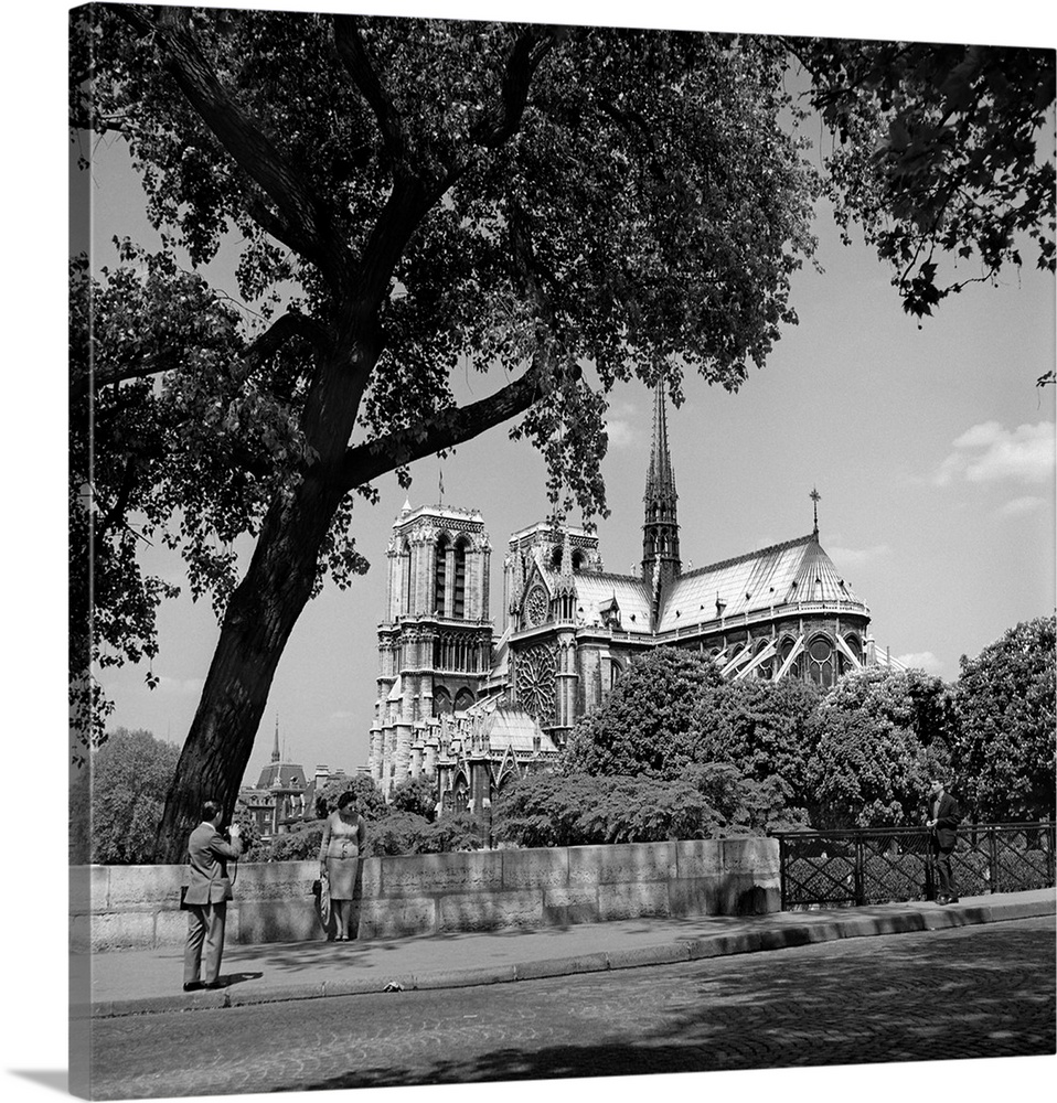 1950's Paris France Tourist Couple Man With Camera Photographing Woman Notre Dame Cathedral In Background.