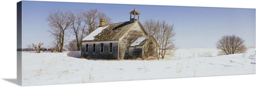 A run down building is surrounded by snow covered land and bare trees.