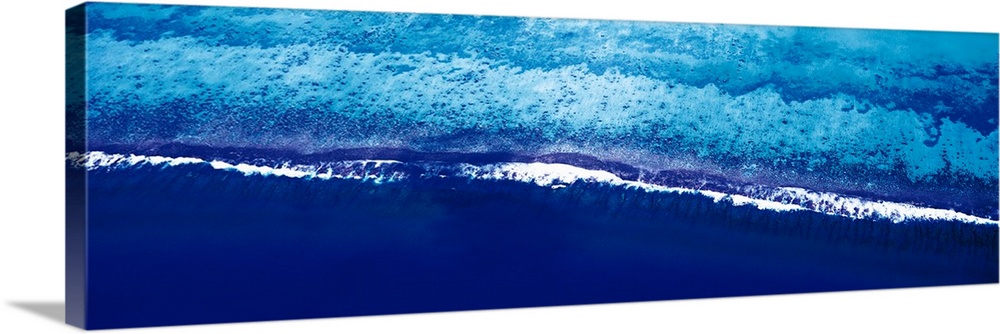 This is a panoramic photograph taken from above of waves breaking on the shore of this tropical reef.