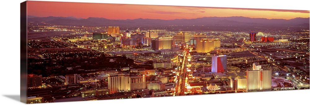 Wide angle, aerial photograph of Las Vegas, lit up at night, mountains in the distant background.