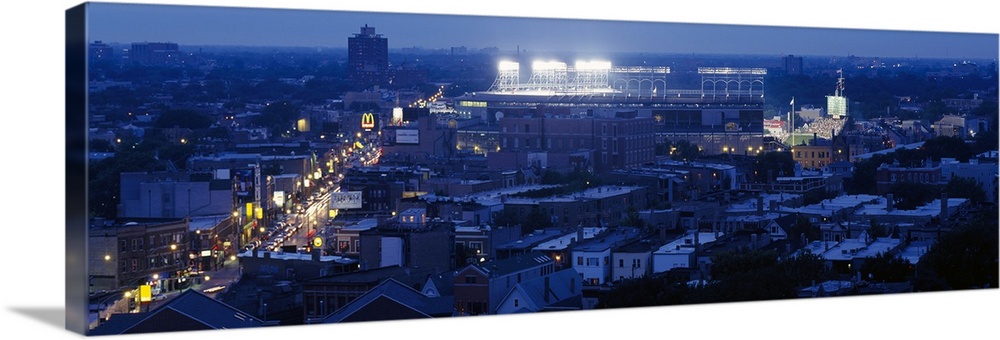 This high angle photograph is taken from a distance but focused on the Chicago Cubs stadium as it's illuminated for a nigh...
