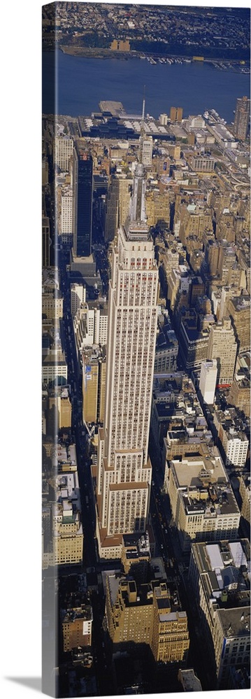 A long vertical picture taken from above the Empire State building which towers over the city surrounding it.