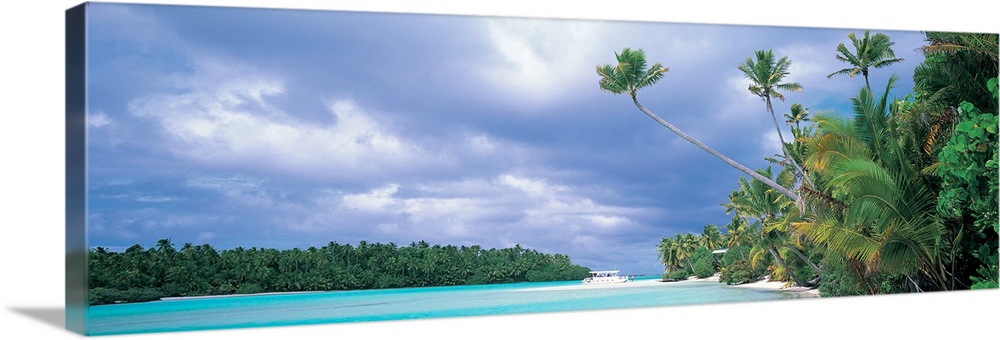 Panoramic photograph of lagoon with shoreline full of trees and tree covered island in distance under a cloudy sky.