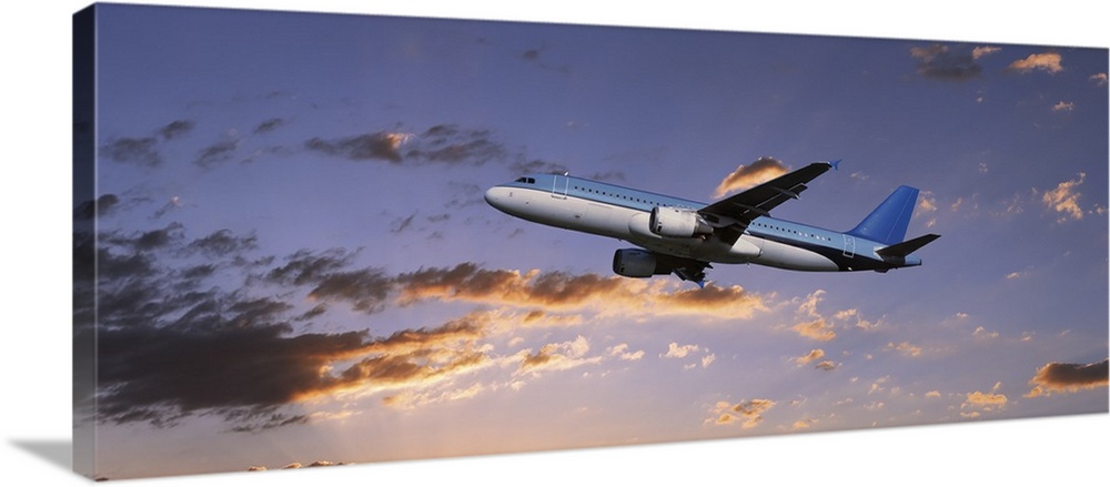 A commercial airplane is pictured from below as it soars through a sunset lit sky.