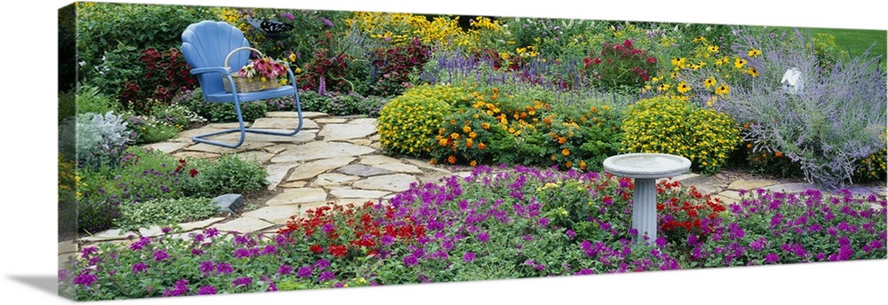 Oversized, horizontal photograph of many types of vibrant flowers and green foliage in a flower garden.  A stone path in t...