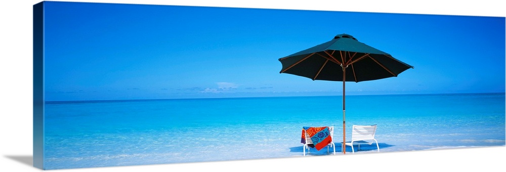 Two beach chairs under an umbrella in front of the ocean in the sand on the Turks and Caicos Islands.