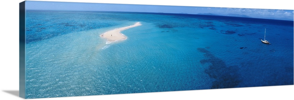 Panoramic, aerial photograph of clear blue waters over the Great Barrier Reef, a single sailboat in the water, in Queensla...