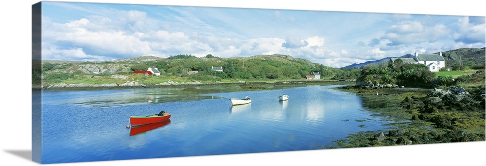 Panoramic photograph of canoes in the water with land and houses in the distance under a cloudy sky.