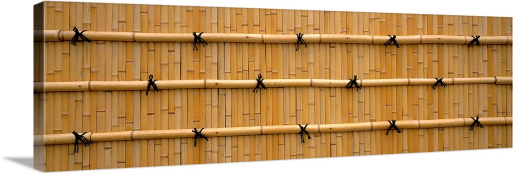 Oversized landscape photograph of a wall constructed entirely of golden bamboo rods and small ties in Kyoto, Japan.