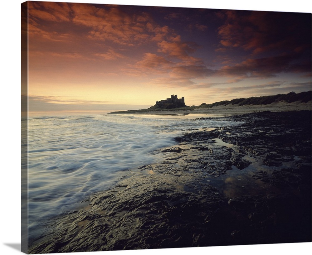 Oversized landscape photograph of a rocky shoreline in England at sunset, Bam burgh Castle can be seen in the distance.