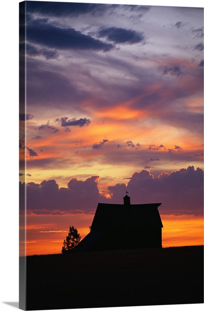 Vertical panoramic photograph of farm house silhouette at dusk under a cloudy and colorful sky.