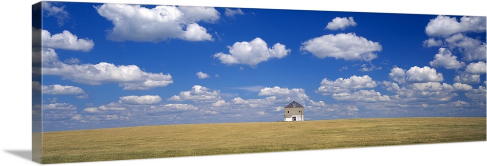 A single house is photographed from a distance as it sits on vast open land underneath a cloud filled sky.