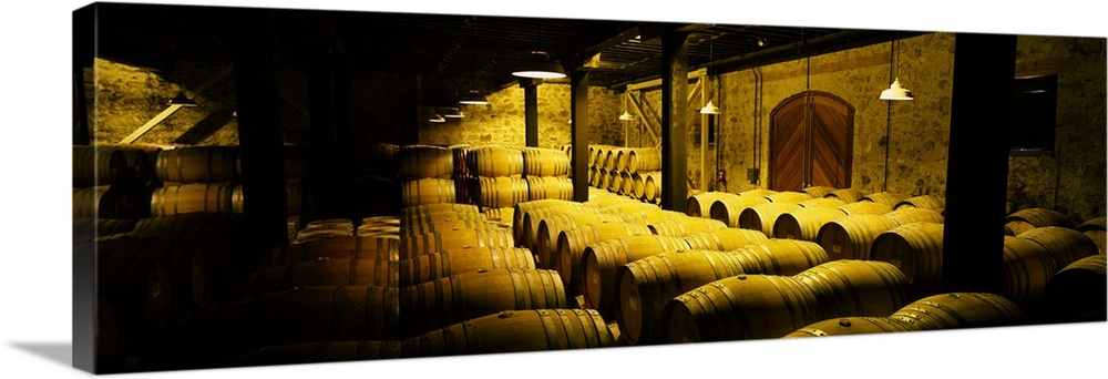 Large, landscape photograph of a partially lit cellar with stone walls, full of wine barrels, in Mt. Veeder, Napa Valley, ...