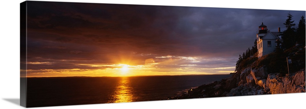 Large panoramic shot of a sun setting over a harbor with a house on a cliff just to the right.