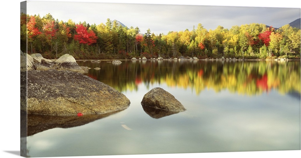 Landscape photograph of a calm body of water with large rocks breaking through the surface around the edges, on the horizo...