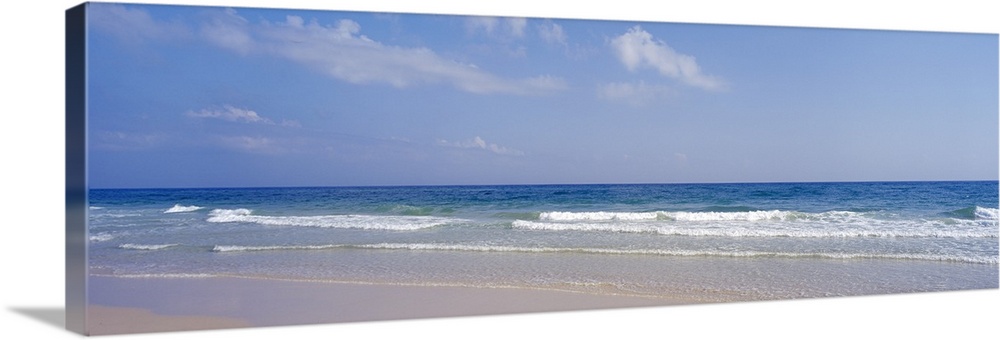 Docor perfect for the home or office of a panoramic shot of a beach with waves coming in and a soft blue sky just above.