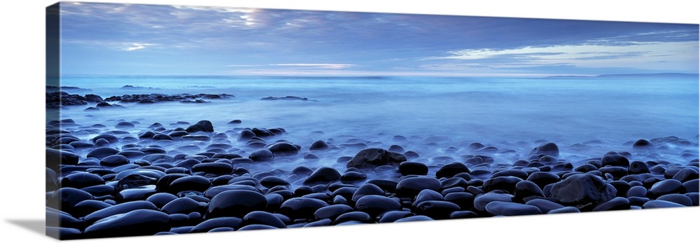 Panoramic photograph shows the shores of a beach in the United Kingdom filled with smooth stones as the water slowly break...