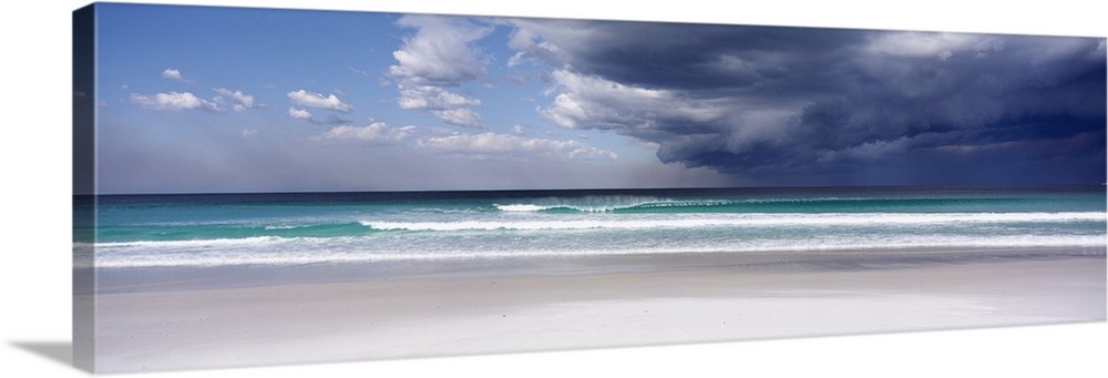 Panoramic photo print of an ocean with crashing waves and blue skies on the left and storm clouds on the right.