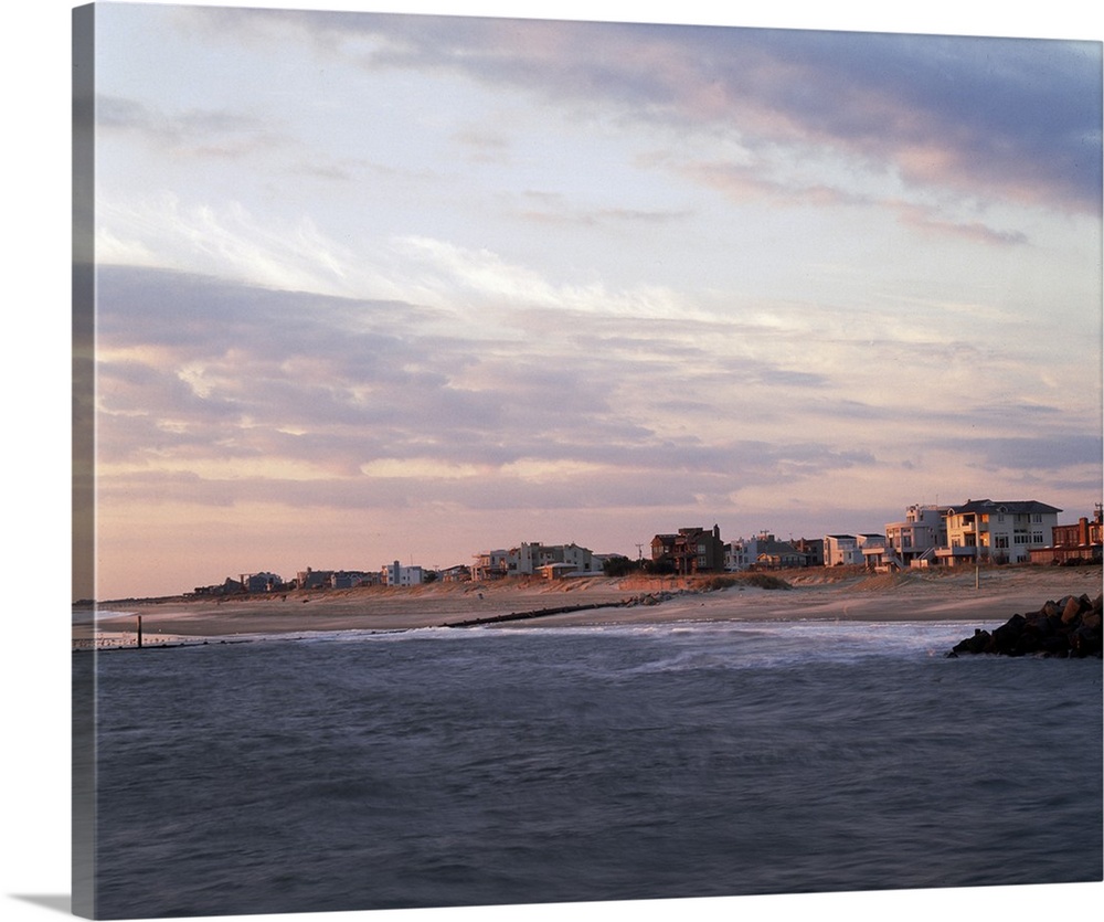 This large piece is a photograph taken on the water looking at the beach coast that is lined with houses.