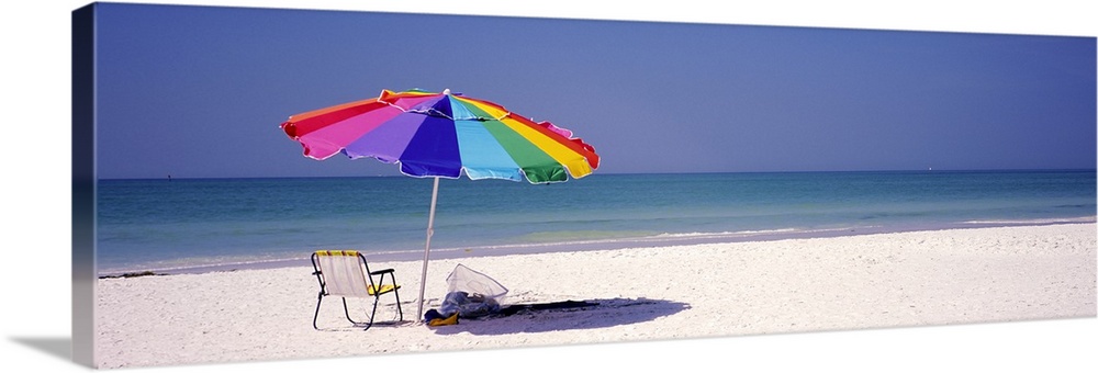 Panoramic photograph of beach chair and parasol in the sand, with ocean fading into the distance.  The sky is clear.