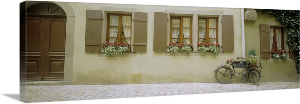 Panoramic photograph of home with huge wooden arched door, windows, shutters, and flowerboxes.