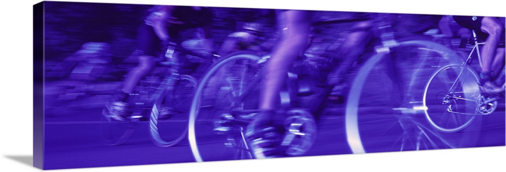 A panoramic photograph taken of cyclists as they race down a street in competition.