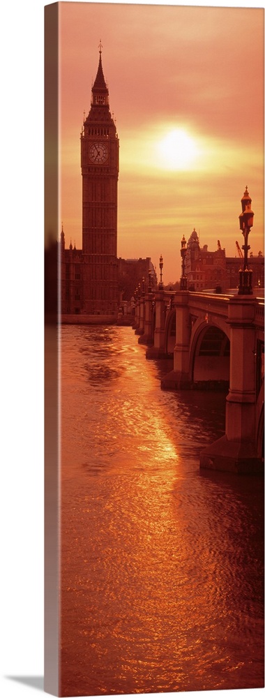 A vertical panoramic photograph taken of Big Ben from across the bridge and over a body of water. The sun is low in the sk...