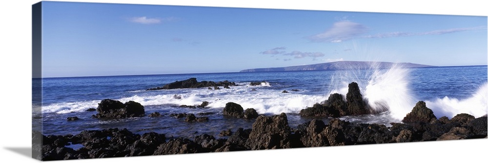 This panoramic photograph shows a wave breaking on the volcanic rock on the island shore.