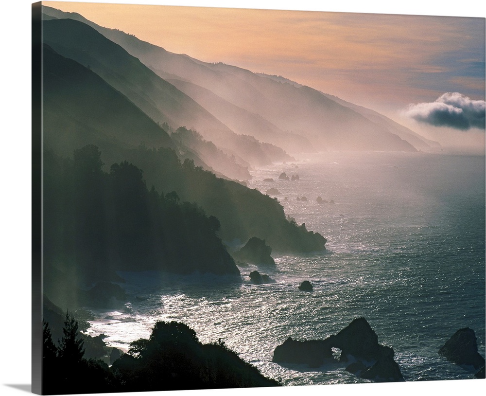 Photograph of the Santa Lucia Mountains rising through fog and mist from the Pacific Ocean.  The sky is warm with clouds i...