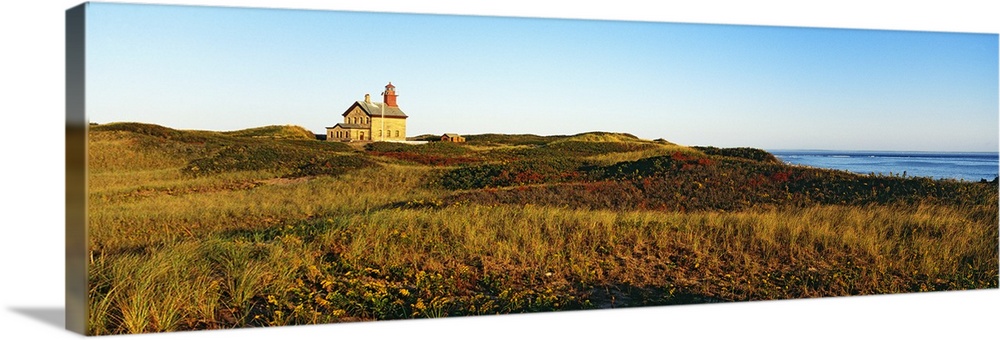 A large lighthouse is photographed in panoramic view surrounded by open grassy land.