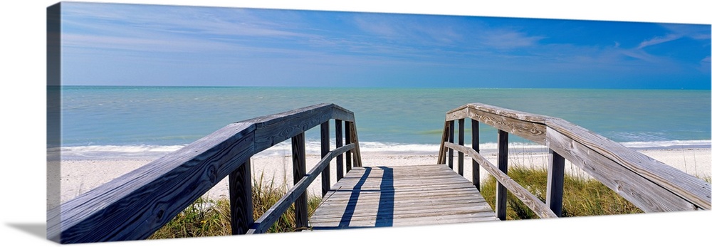 Wall art for the home or office this panoramic photograph shows a boardwalk over dunes to a sandy shore and calm ocean.
