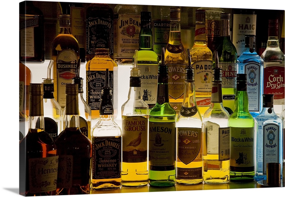 Photograph of glass bottles full of different kinds of alcohol such as Jack Daniels, Powers, Famous Grouse, and Jim Bean.