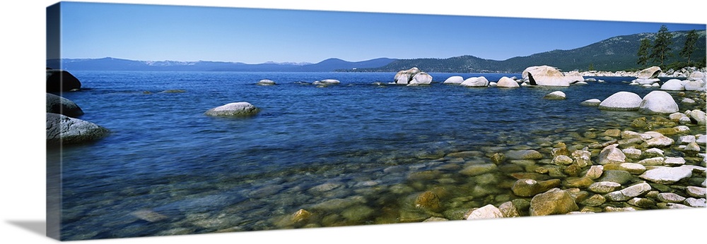Panoramic view of Lake Tahoe with a line of rocks on the bottom and toward the right side of the picture. Mountains are sh...