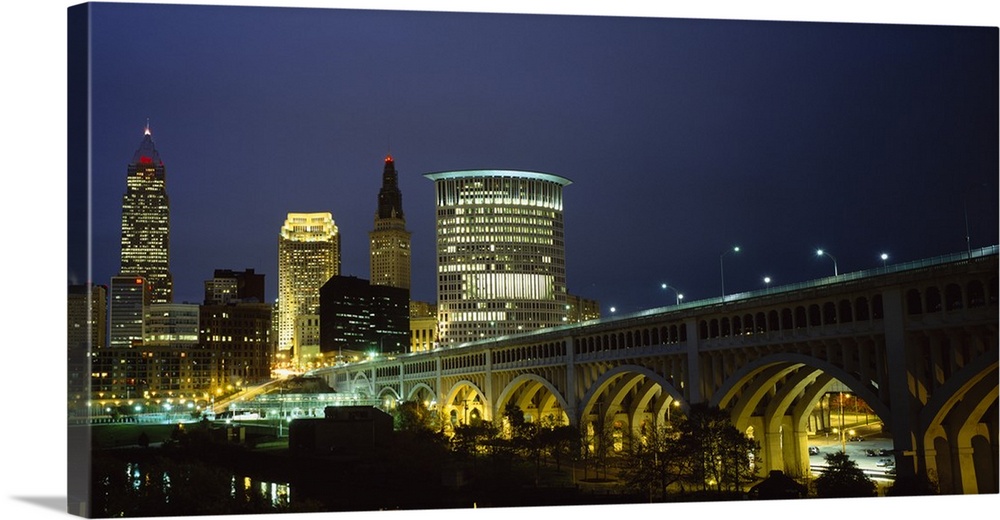 Panoramic photograph of overpass leading to a lit up collage of buildings at dusk.