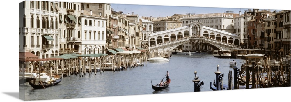 Panoramic photograph taken of a walking bridge over a canal in Italy with gondola boat docks lining both sides of the water.