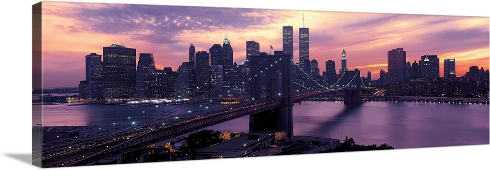 This wall hanging is a panoramic photograph captures the fading sun as skyscrapers begin to turn on their lights for the n...