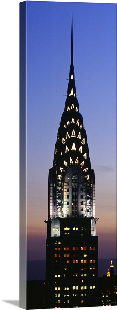 Vertical, oversized photograph of the top of the Chrysler Building in New York City, lit up against the night sky.