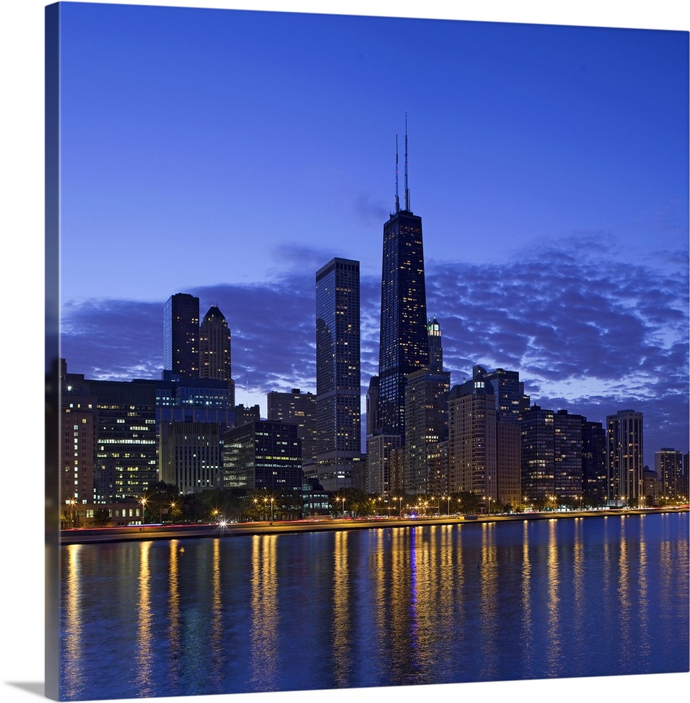 Big, square photograph of the Chicago skyline at night, reflecting in the waters of Lake Michigan.