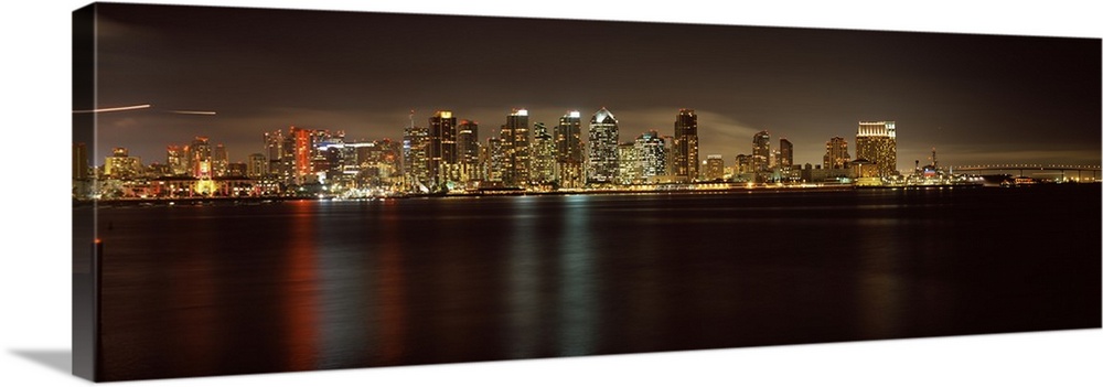 Panoramic photograph of the San Diego city skyline along the edge of the bay in the evening, the waters reflecting the cit...