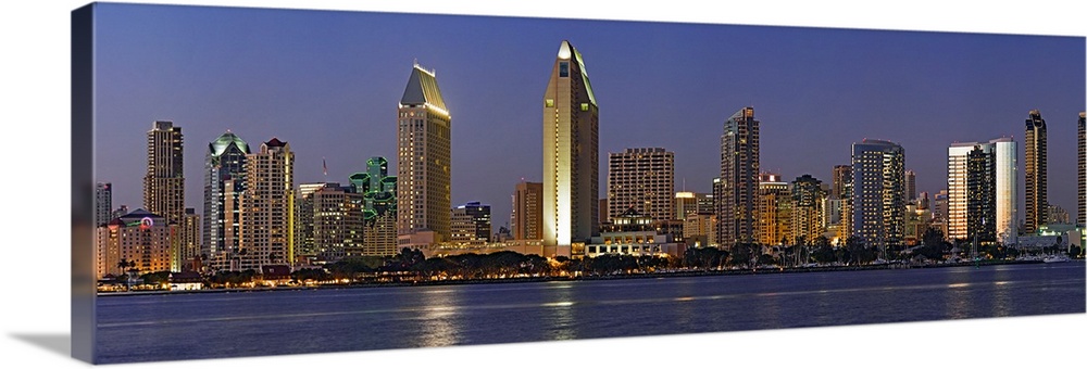 Panoramic photograph of skyline at night with buildings lit up and reflected in the waterfront below.