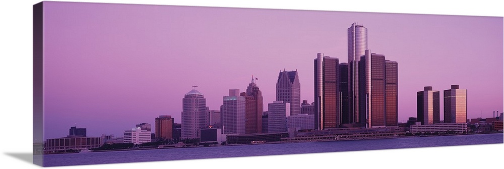 The Detroit skyline is photographed in panoramic view from across the waterfront during dusk.