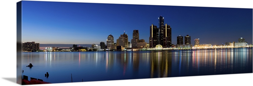 Narrow canvas print of the Detroit skyline illuminated in the evening with it's lights reflecting back on the water.