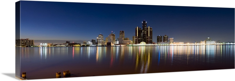 Panoramic photograph of skyline and waterfront at night.  The building lights create colorful reflections in the water.